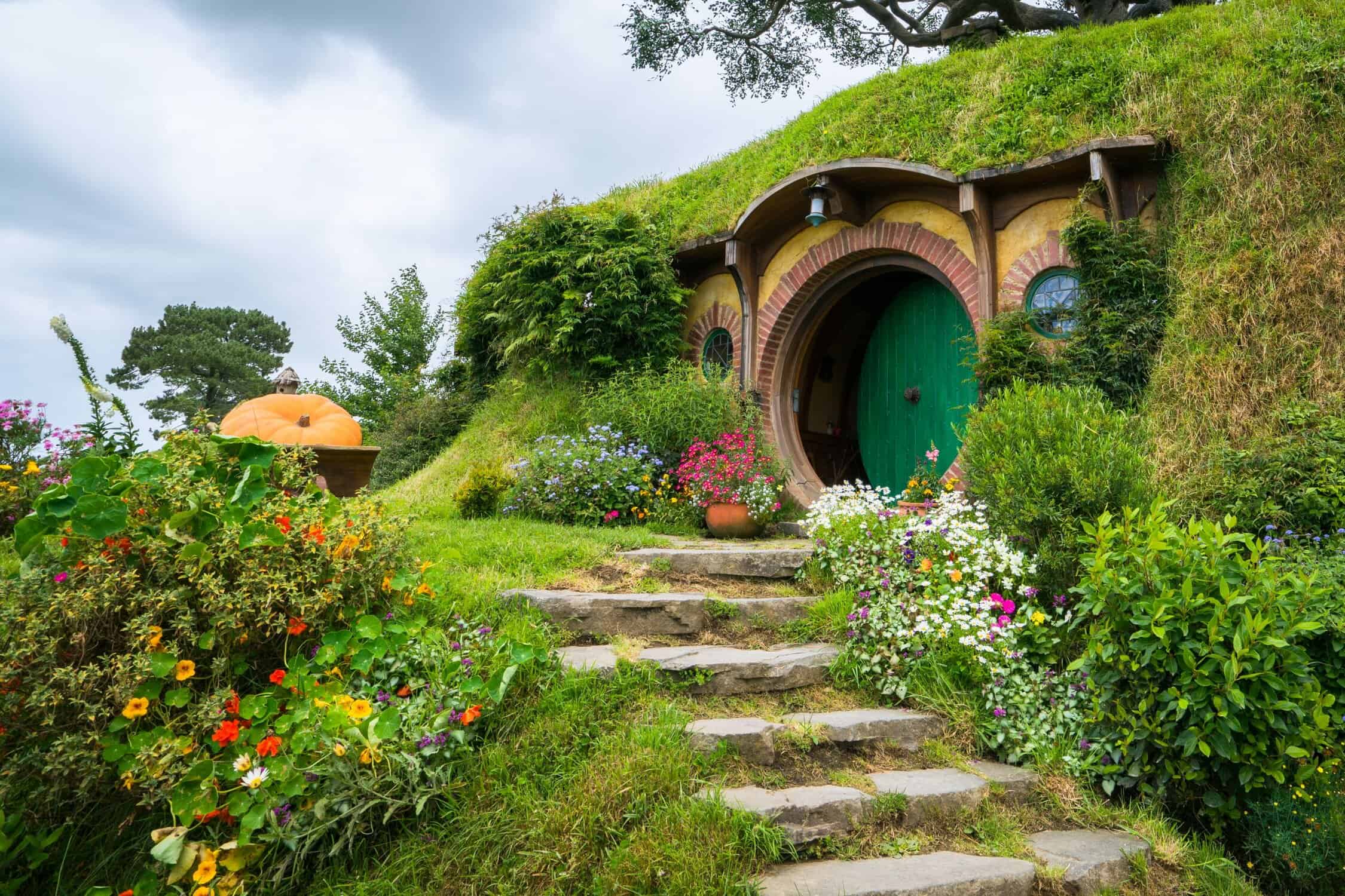The green door of a hobbit hole at the Hobbiton Movie Set, surrounded by cottage gardens