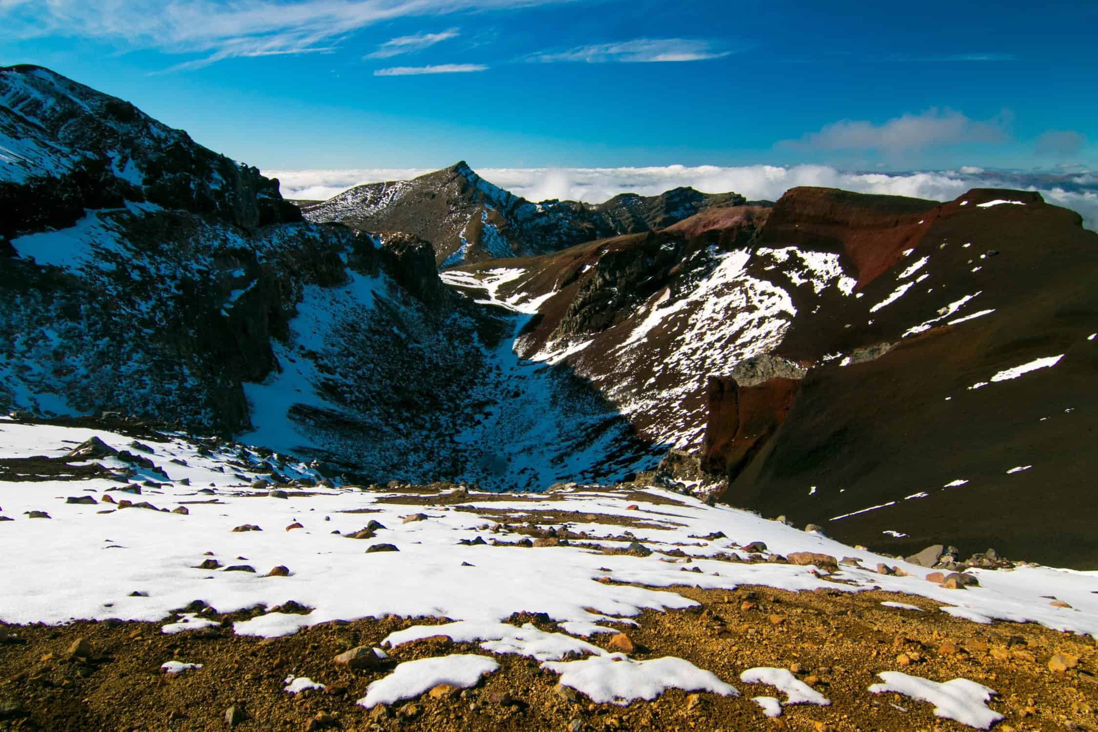 Snow-dusted red volcanic crater and ridgeline on Mount Tongariro above the clouds